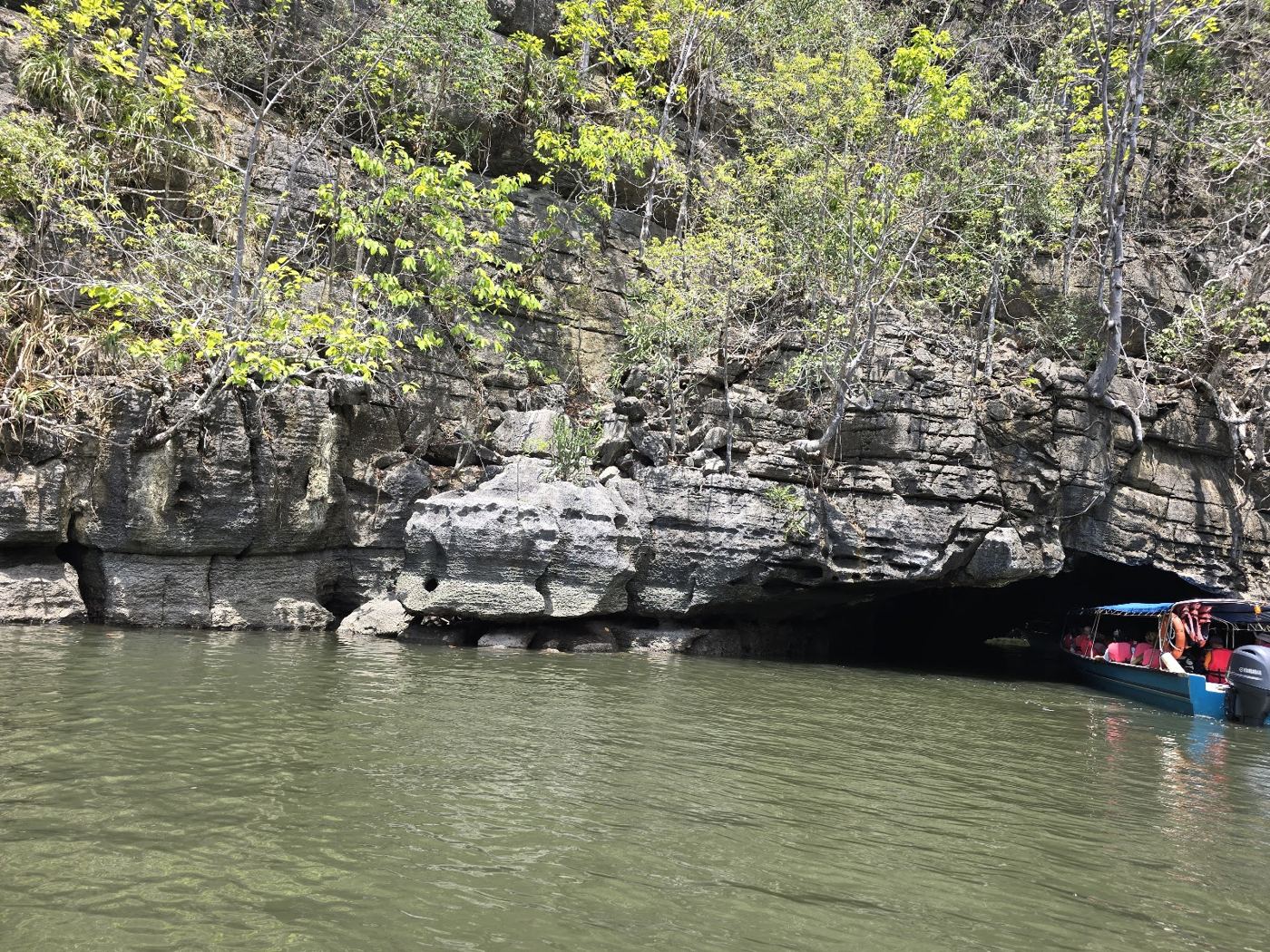 Tour boat entering a cave under limestone cliffs